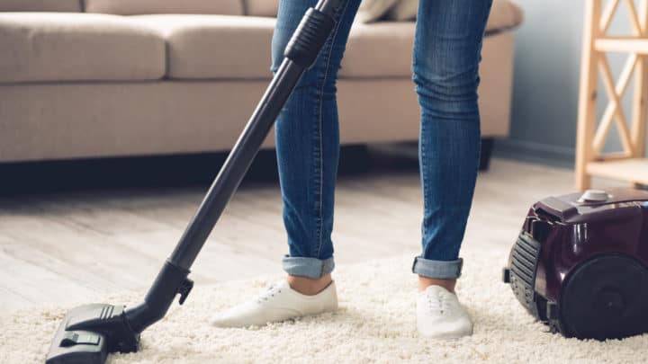 Cropped image of woman in jeans using a vacuum cleaner while cleaning her house